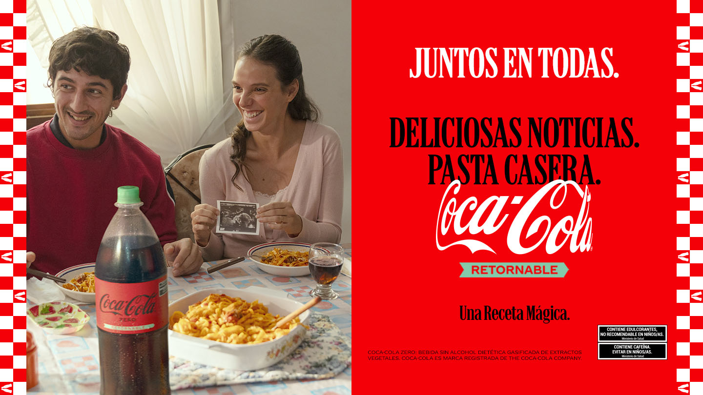 Pareja feliz disfrutando de una comida casera con Coca-Cola, sosteniendo una imagen de una ecografía.