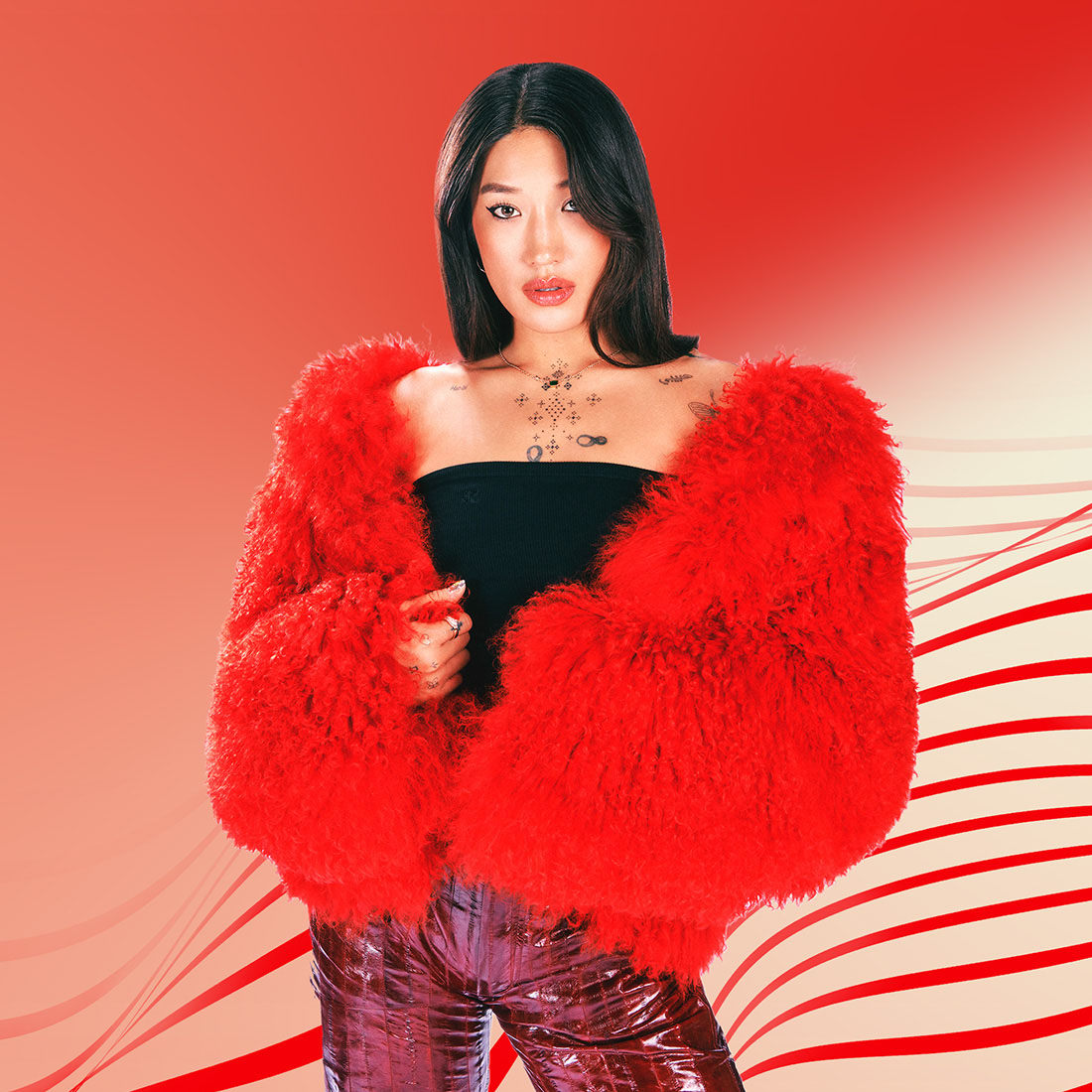 Peggy Gou posando con una chaqueta de piel roja frente a un fondo rojo.