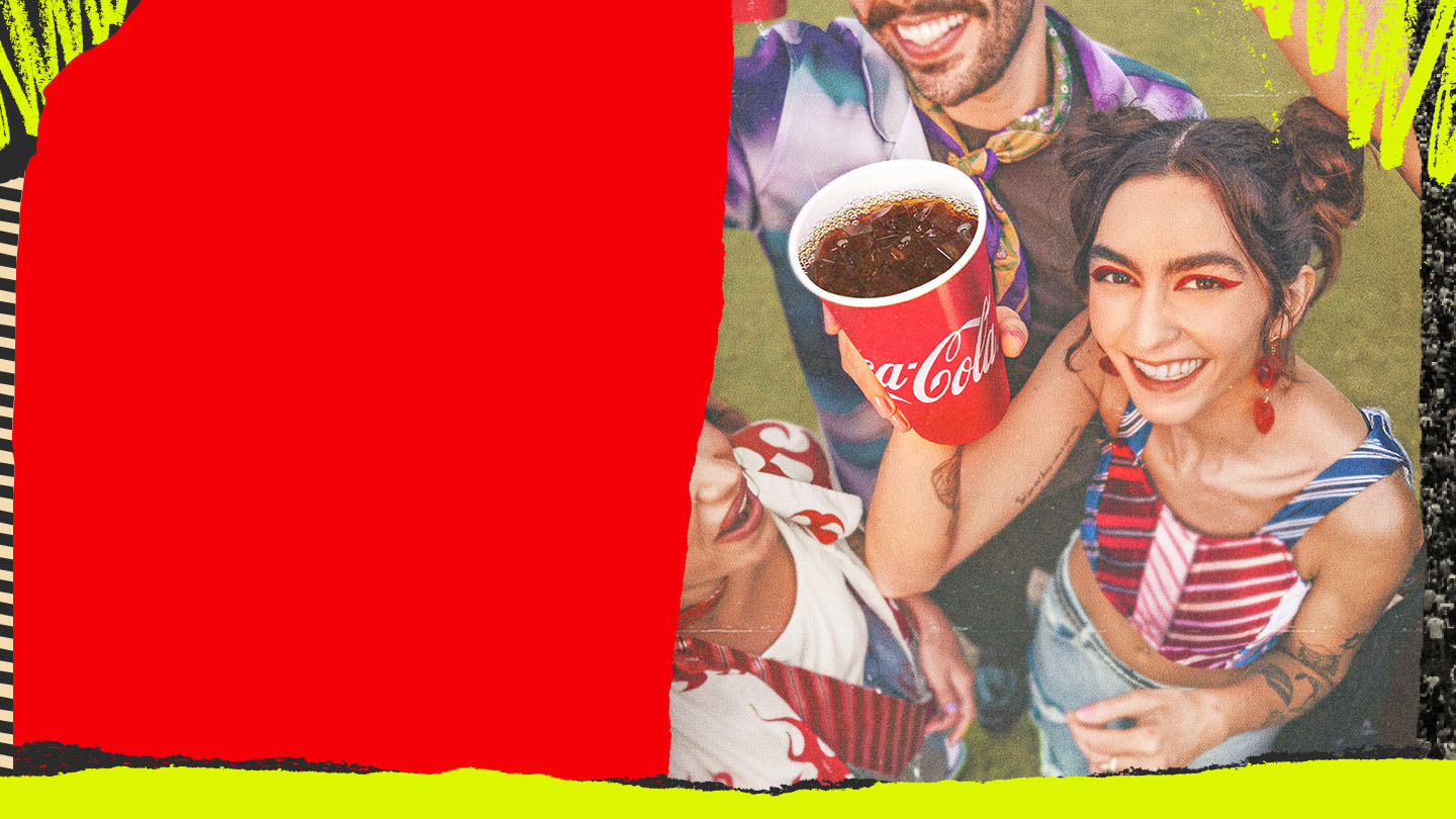 Un grupo de amigos de fiesta por la noche, sosteniendo vasos de Coca-Cola y bailando. Una mujer con el pelo rizado, vistiendo una blusa de patrón floral, está en primer plano riéndose alegremente, rodeada de amigos en un entorno animado y colorido.