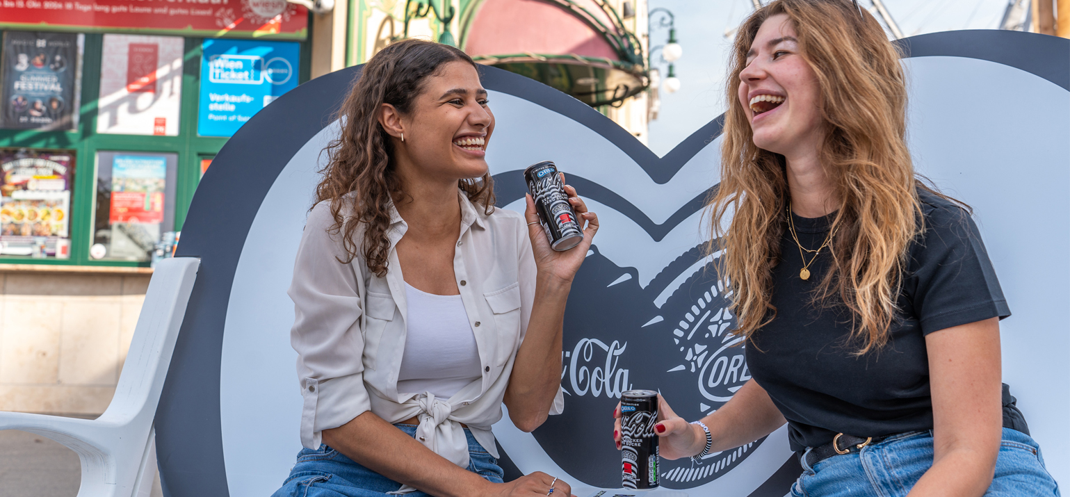 Zwei Personen auf der Bestie-Bank Platz mit dem brandneue Coca-Cola OREO® Zero Sugar