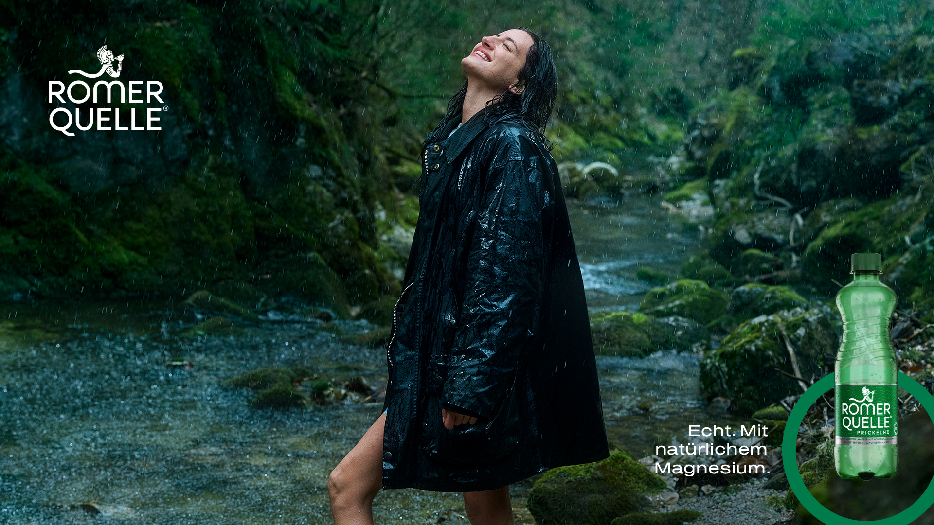 Frau steht lächelnd im Regen in einer grünen Naturlandschaft mit Wildbach, schwarzer Regenjacke, Blick nach oben gerichtet – Römerquelle Prickelnd, Echt. Mit natürlichem Magnesium.