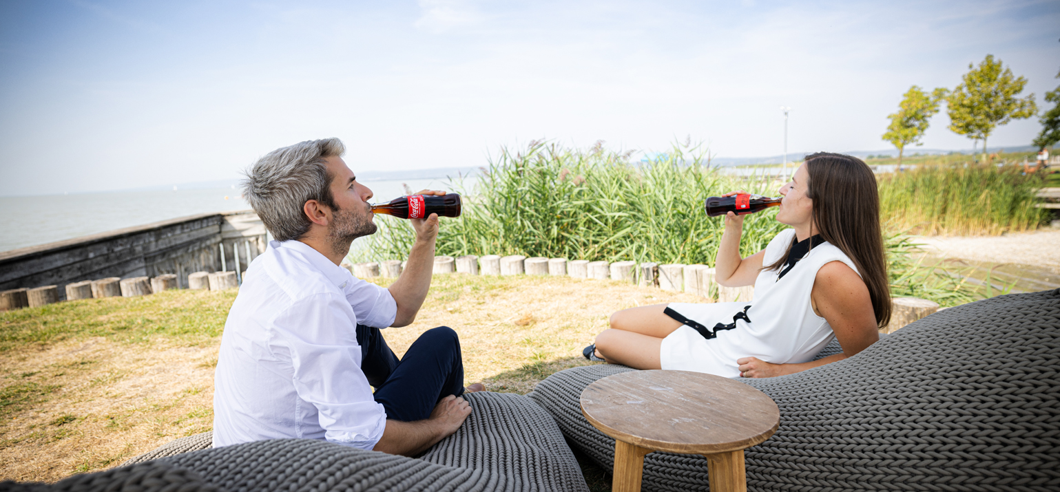 Zwei Personen sitzen gemütlich und trinken Coca-Cola