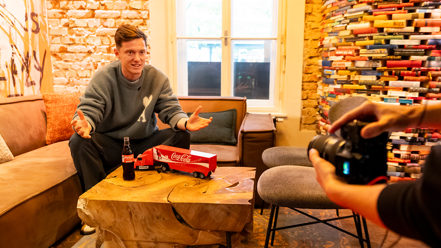 Michael Gregoritsch beim Coca-Cola Meet & Greet 2025 mit Coca-Cola Truck und Glasflasche vor einer Bücherwand.