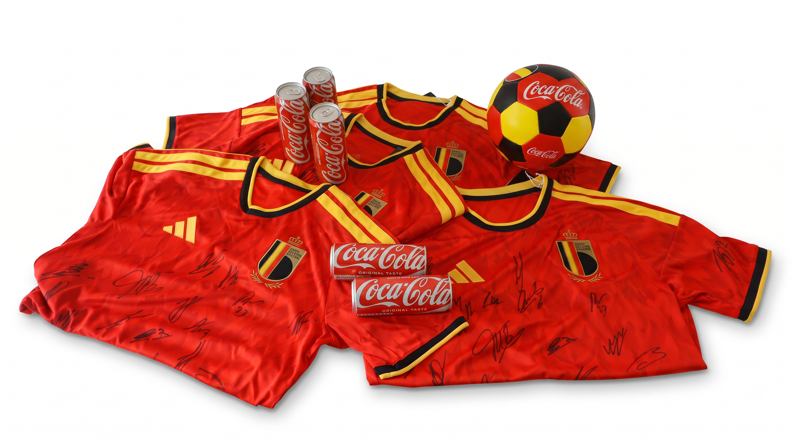 Rode Belgische voetbalshirts met handtekeningen liggen op een witte achtergrond, samen met meerdere Coca‑Cola blikjes en een voetbal in Belgische kleuren met Coca‑Cola‑logo.