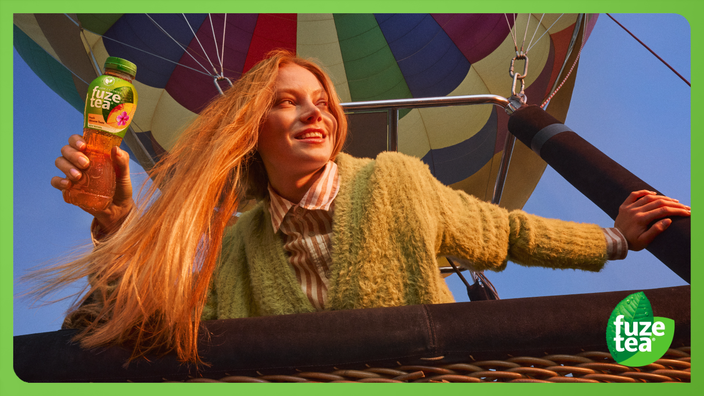 Jonge persoon die zich in heteluchtballon bevindt die een fles fuze tea drinkt