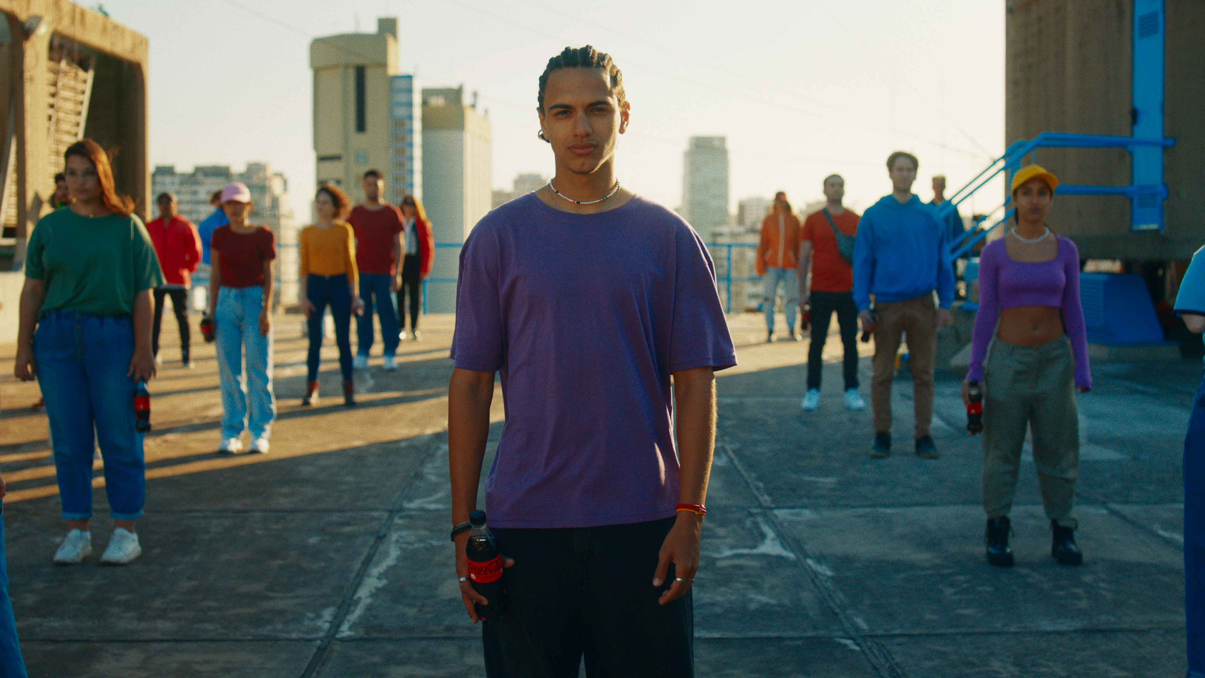 Jóvenes con remeras de distintos colores, están paradas mirando en una misma dirección con botellas de Coca-Cola en sus manos