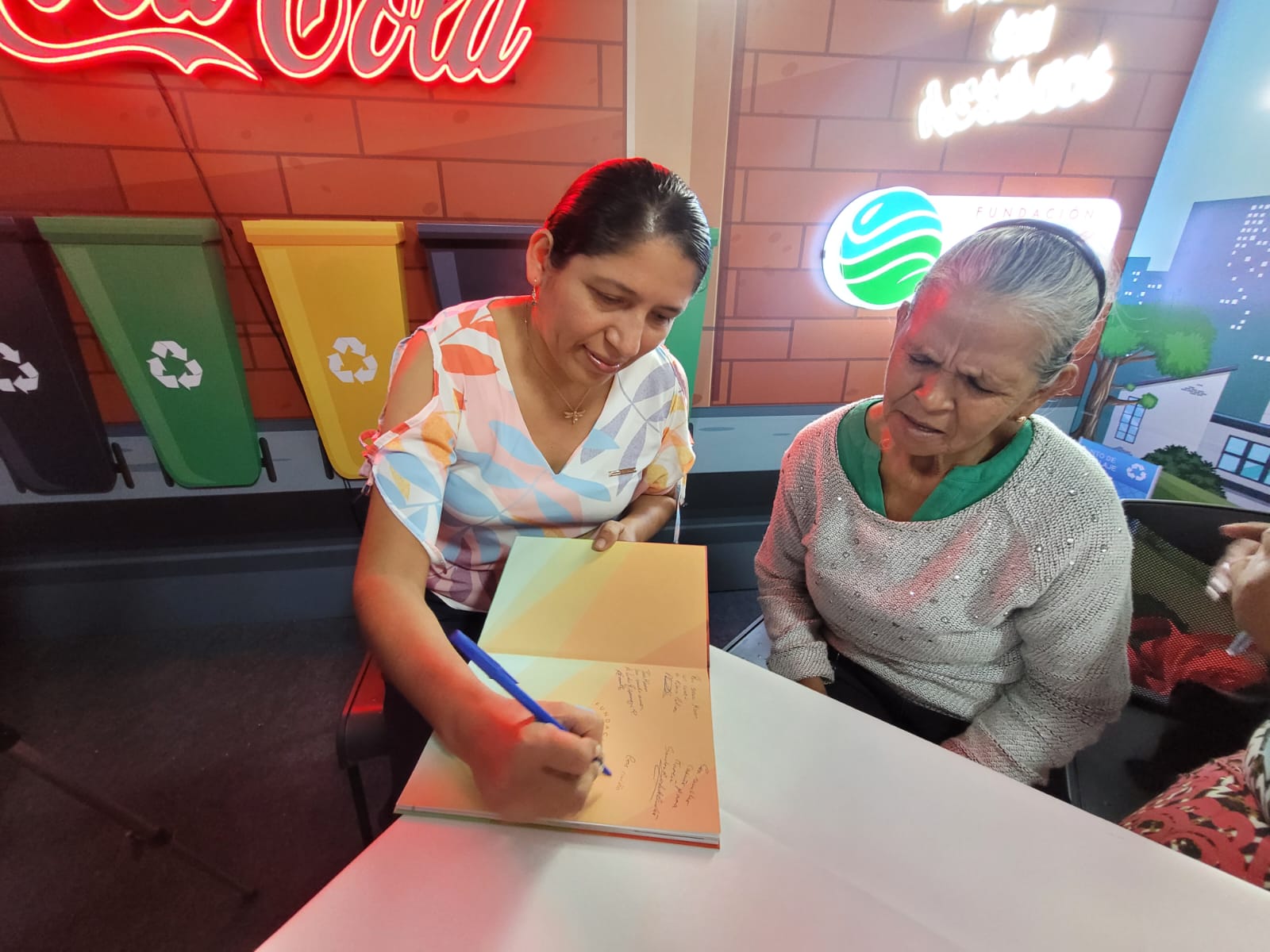 dos mujeres sentadas autografiando un libro