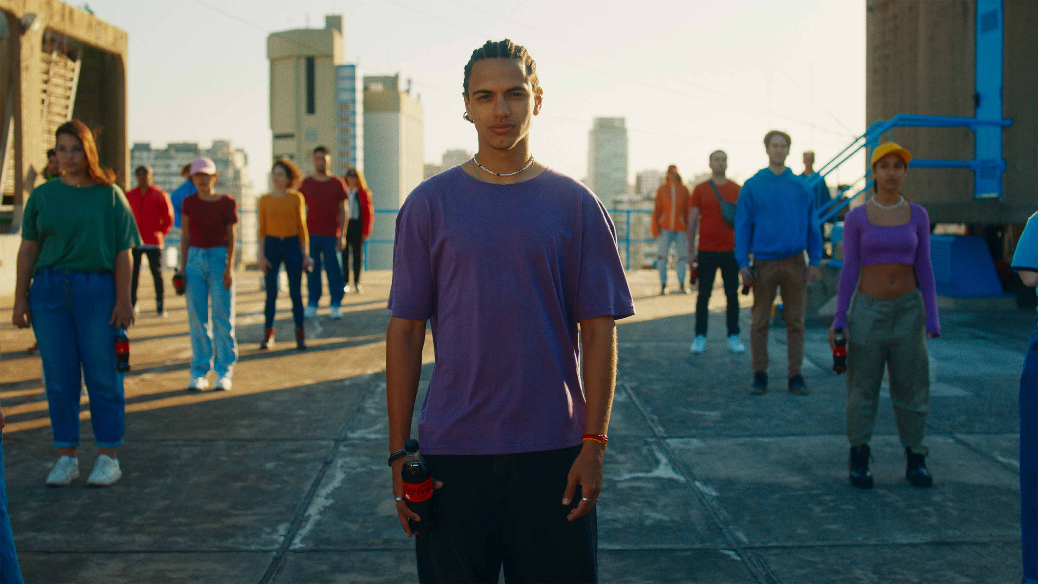 Jóvenes con remeras de distintos colores, están parados mirando hacia adelante, con botellas de Coca-Cola en sus manos