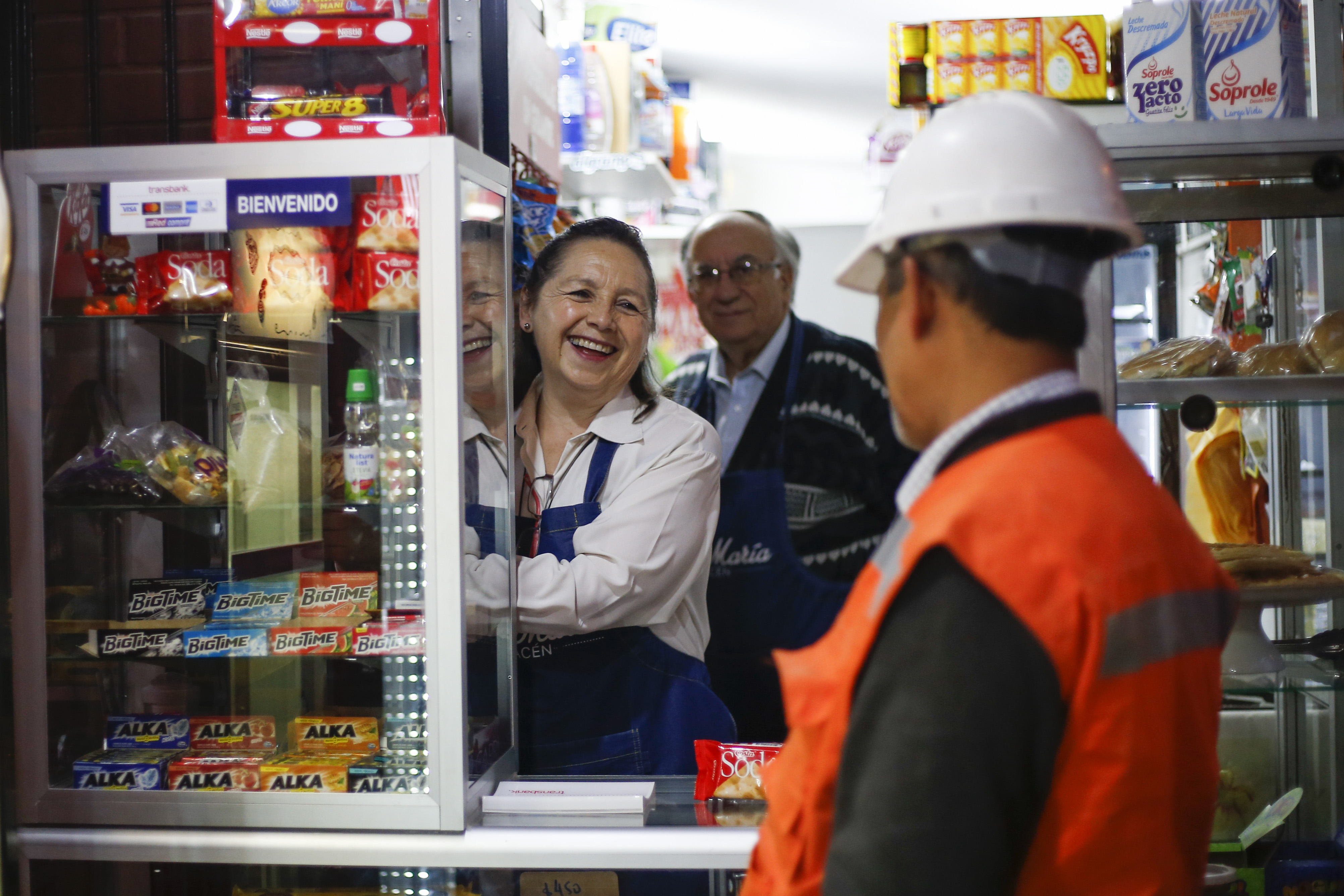 Tres personas conversan, en una tienda de barrio