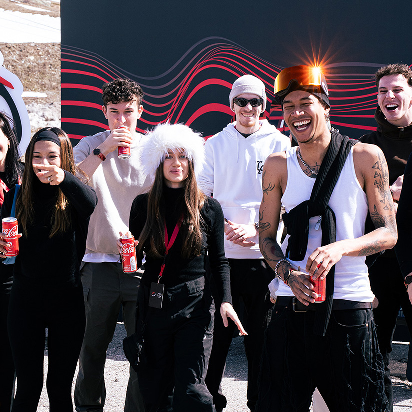 Um grupo de jovens sorridentes desfrutando de Coca-Cola em um ambiente de inverno, com roupas quentes e óculos de sol.