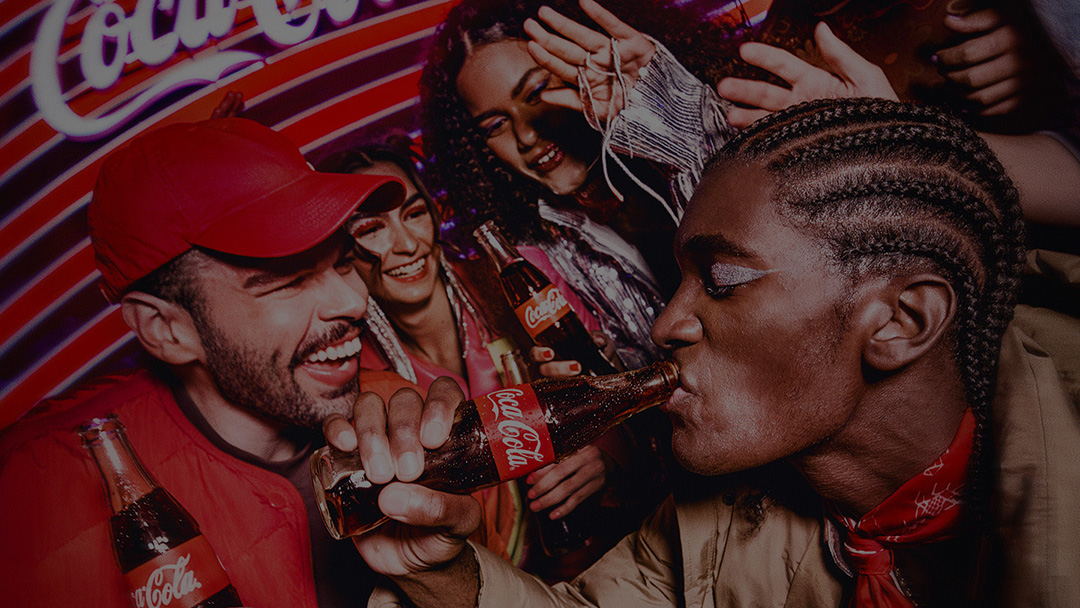 Grupo de amigos se divertindo com garrafas de Coca-Cola em uma festa animada, com sorrisos e cores vibrantes.