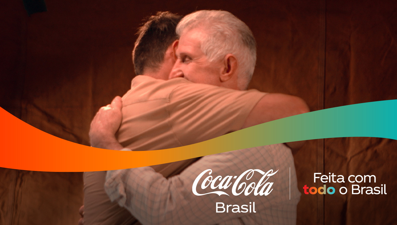 Dois homens se abraçam, com logos da Coca-Cola Brasil e a frase "Feita com todo o Brasil" em destaque.