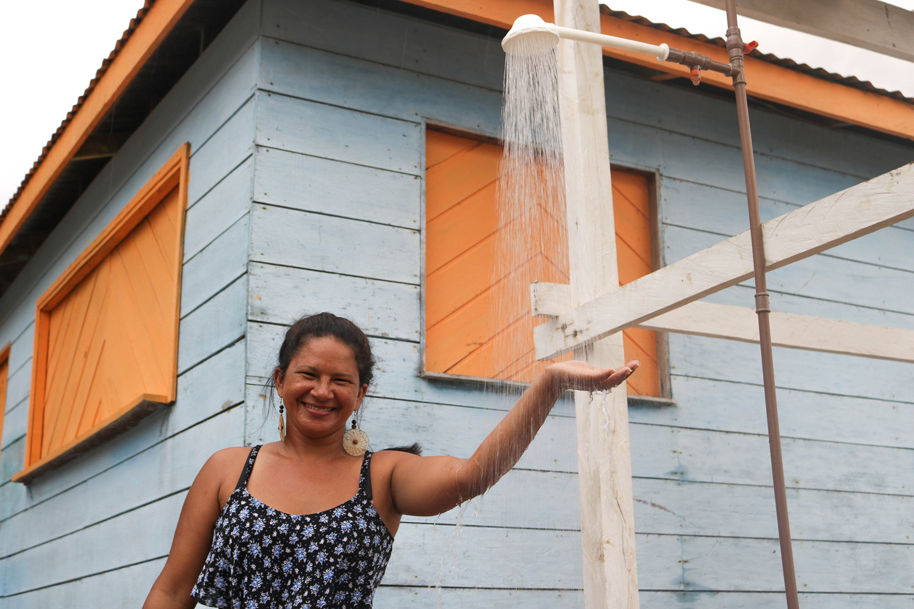 Mulher sorrindo e esticando a mão em um chuveiro ao ar livre.