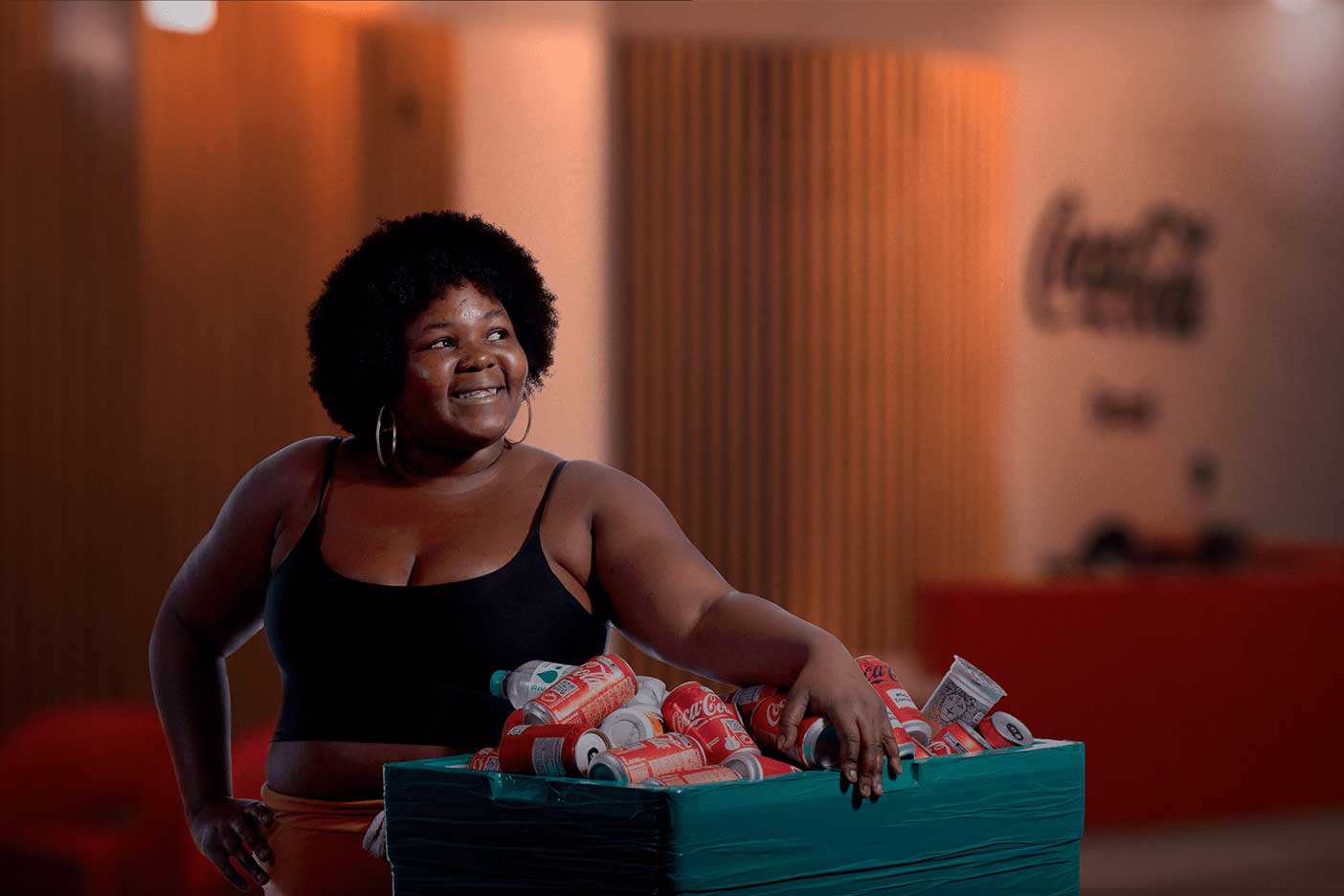 Mulher posando em uma sala de Coca-Cola e segurando uma lixeira com latas de Coca-Cola e copos de Chas Leão