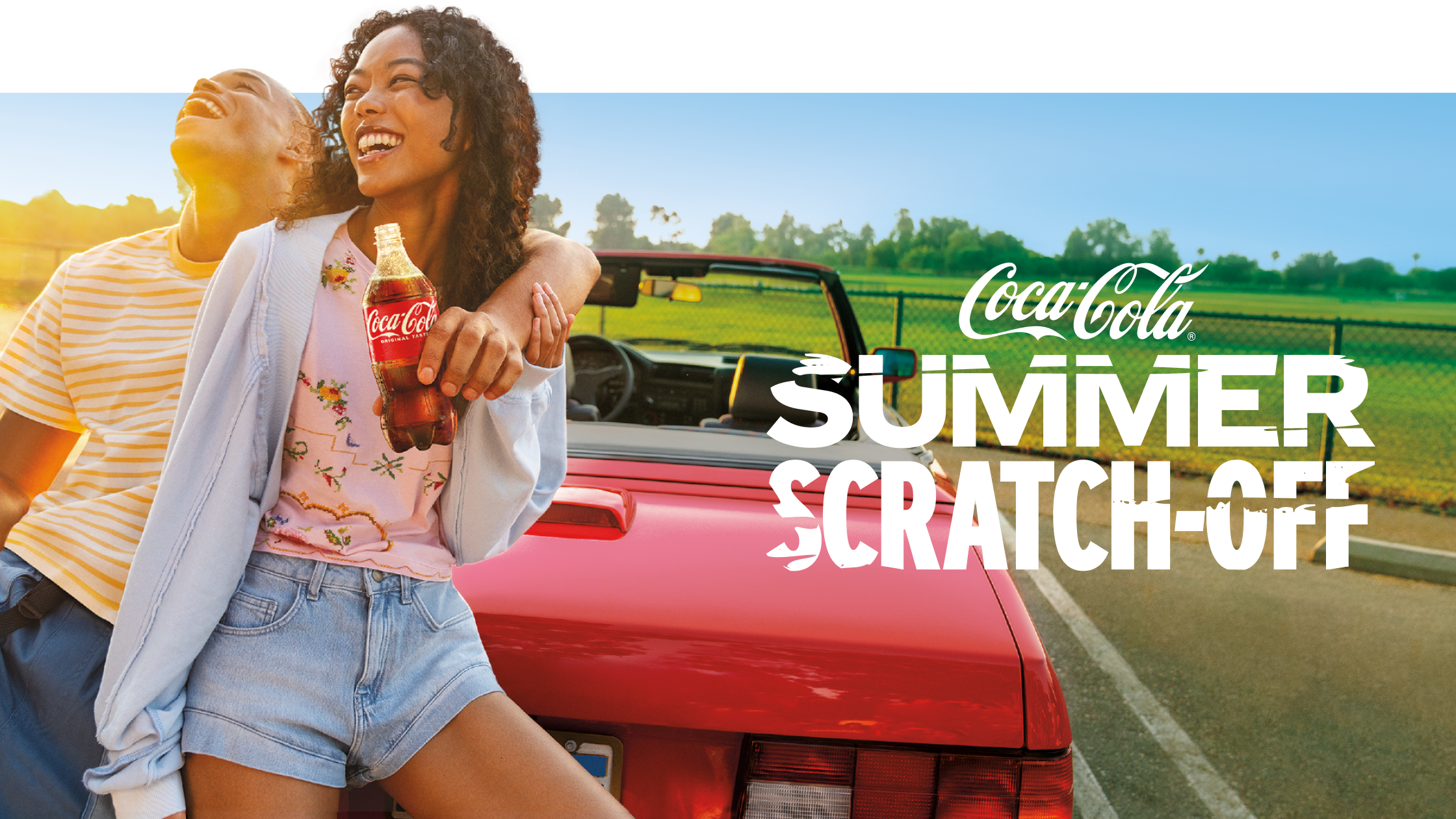 A happy couple enjoys a sunny day with a bottle of Coca-Cola by their red convertible for the Summer Scratch-Off promotion.