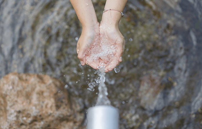 Une main faisant une coupe pour recueillir de l'eau au bout d'un tuyau