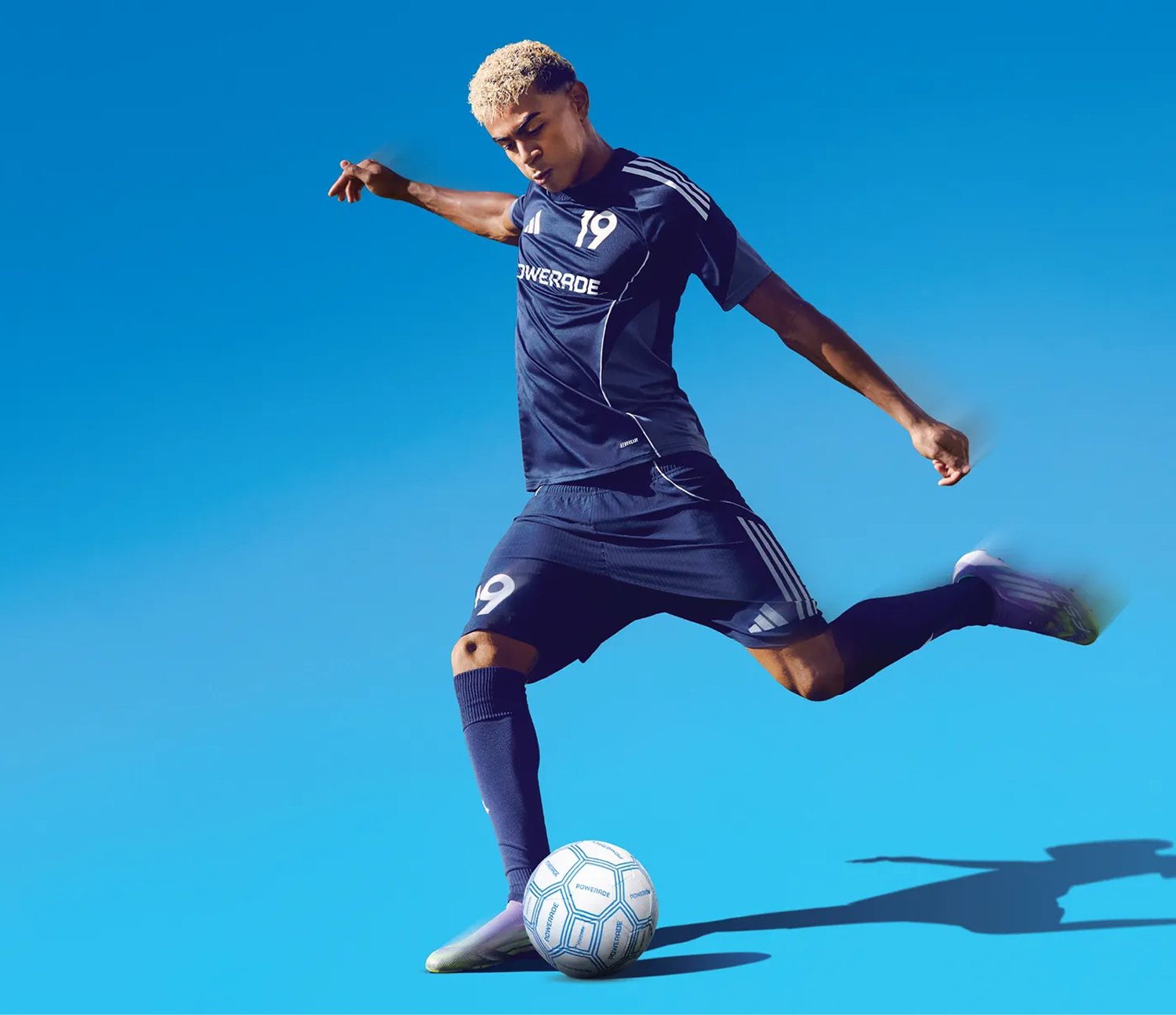 Joueur de soccer en uniforme bleu marine frappant un ballon sur fond bleu vif pour une campagne Powerade FIFA.