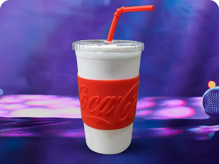 Un gobelet réutilisable avec un manchon de marque Coca-Cola, un prix du lot Moments festifs, sur fond violet.