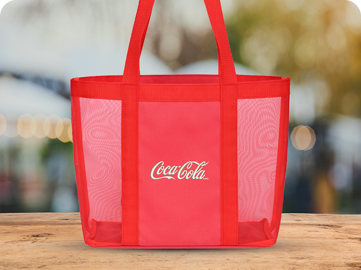 Un sac fourre-tout en maille rouge vif de Coca-Cola, un prix du lot Activités en plein air, posé sur une surface en bois.