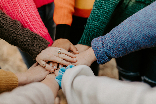 Un groupe de personnes portant des chandails tricotés colorés forment un cercle et empilent leurs mains au centre en signe d'unité.