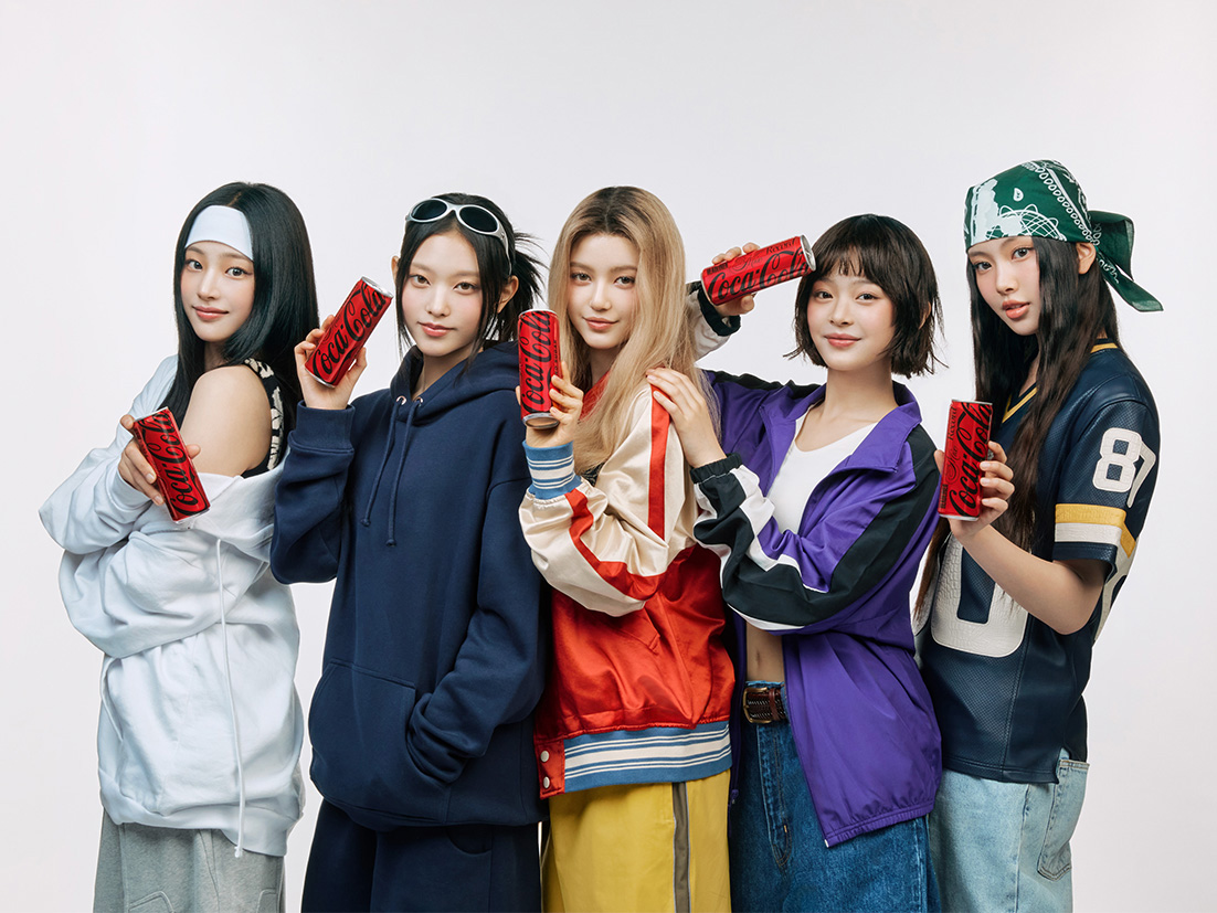 NewJeans posing together, each holding a can of Coca-Cola