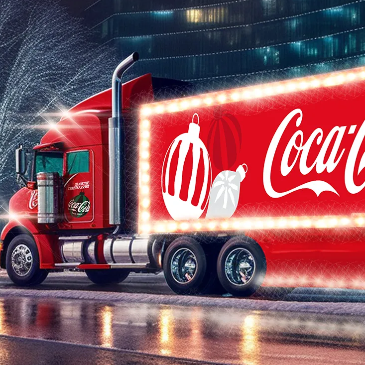 Ein großer Lastwagen ist in festlichem Coca‑Cola‑Weihnachtsdesign, mit Lichtern und Dekorationen, rot gestaltet.