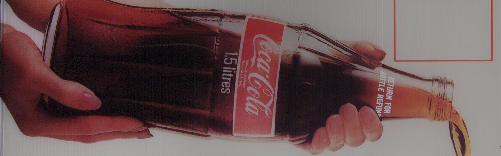Deux mains tiennent une bouteille de Coca-Cola et versent la boisson.