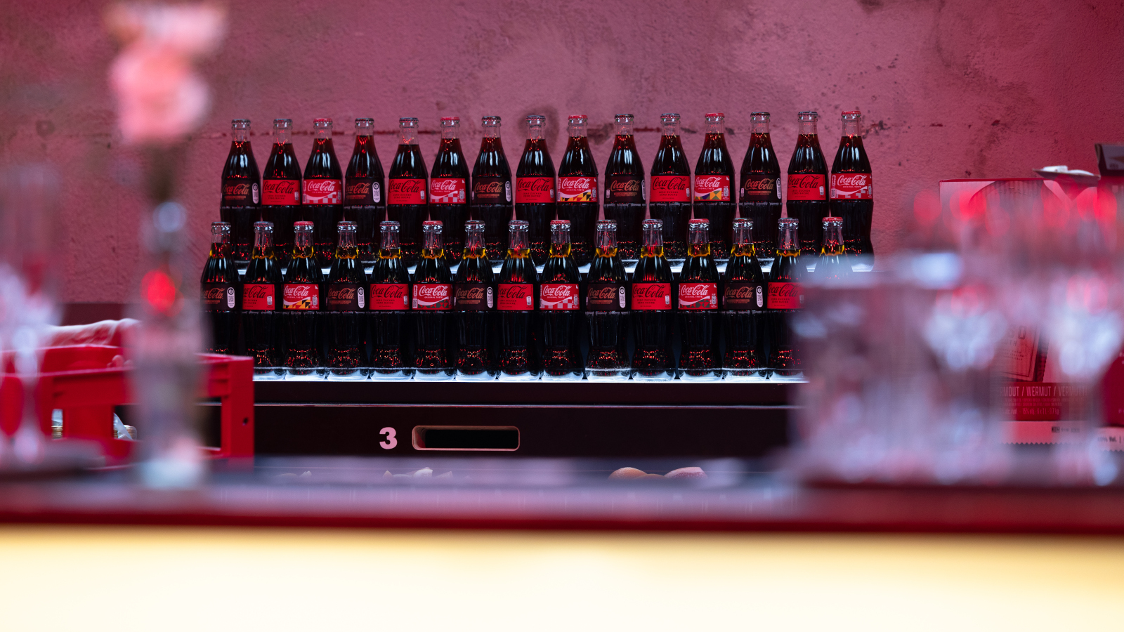 Coca-Cola Glasflaschen stehen vor rotem Hintergrund bei der Jubiläumsfeier.