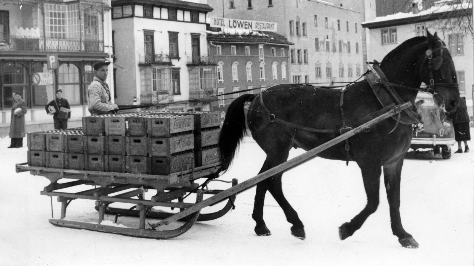 Historische Aufnahme eines Pferdegespanns mit Kisten voller Coca-Cola Flaschen in einer Schweizer Stadt.