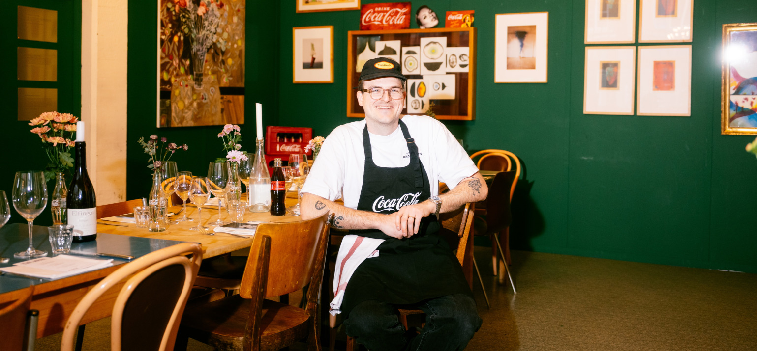 Noah Bachofen is sitting on a chair in front of a green wall
