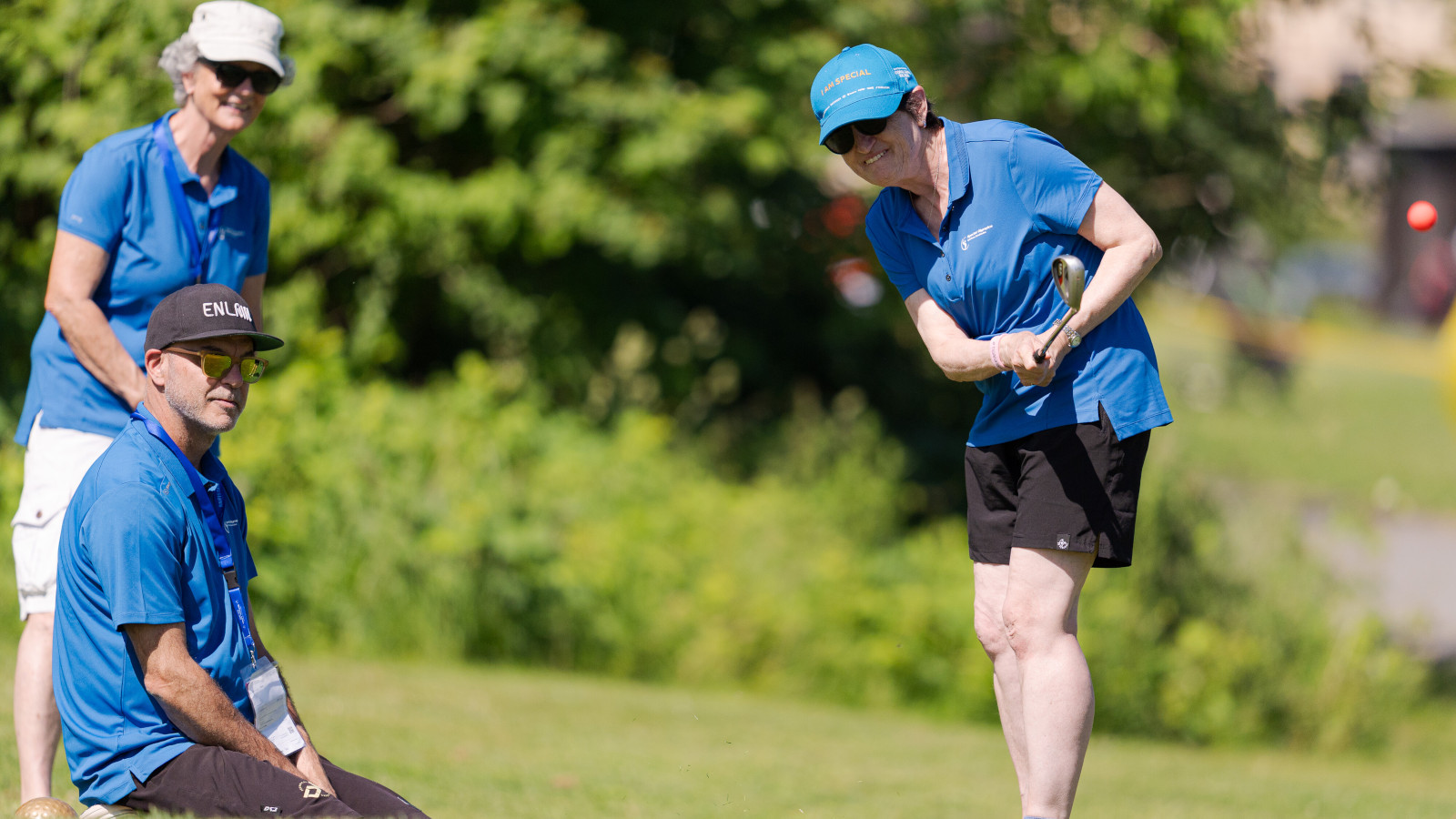 Eine Athletin puttet auf dem Golfplatz, begleitet von zwei Helfenden.