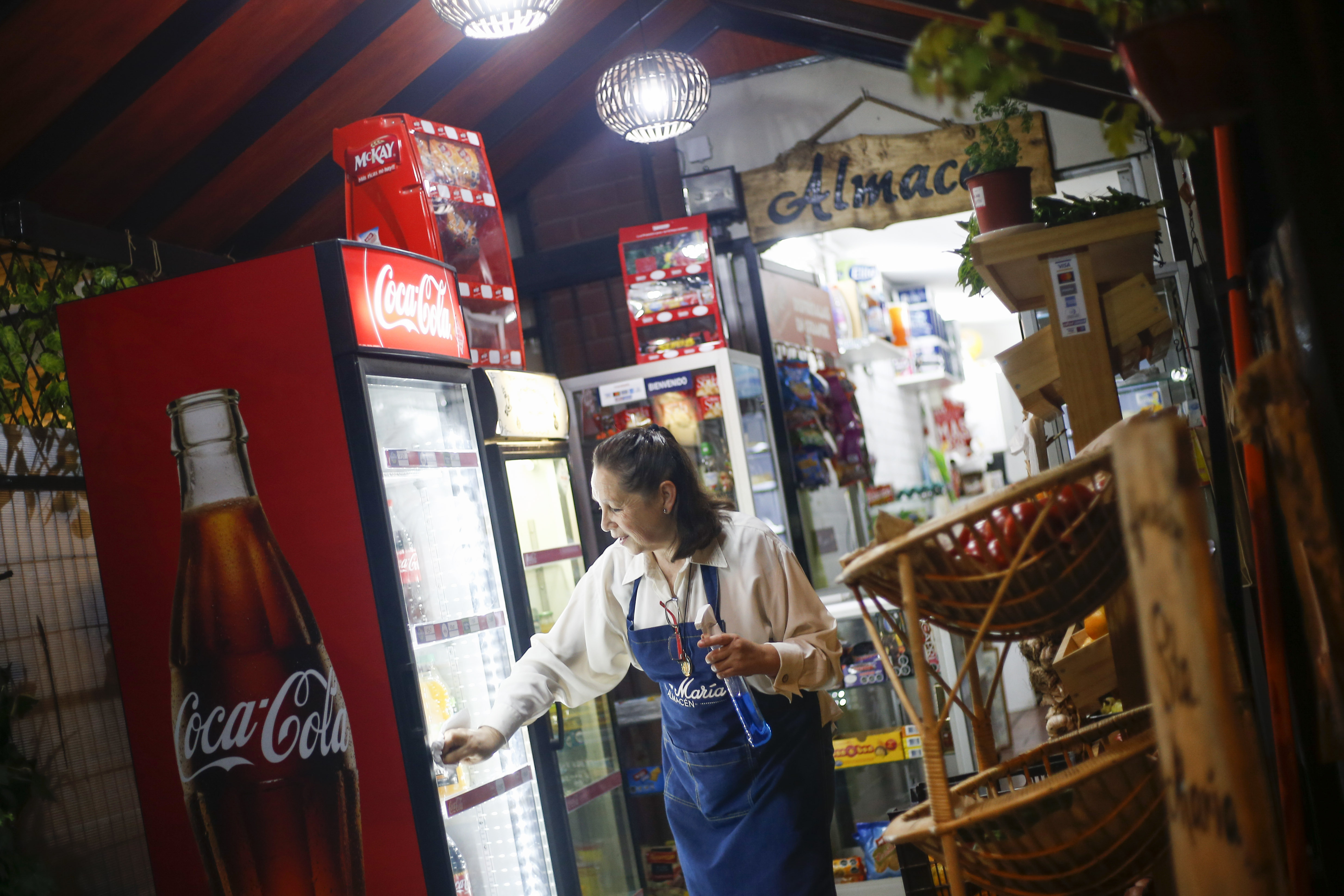 Dueña de un almacén limpia una heladera de Coca-Cola