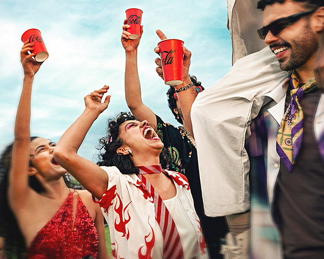 Un grupo de amigos de fiesta por la tarde, sosteniendo vasos de Coca-Cola y bailando.