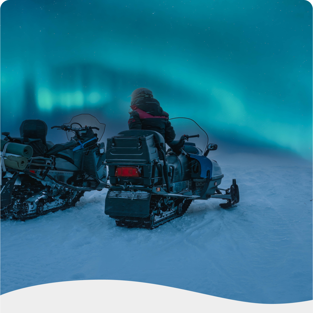 Person sitzt auf einem Schneemobil unter den Nordlichtern