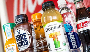 Various bottles of Coca-Cola products in front of a Coca-Cola advertising