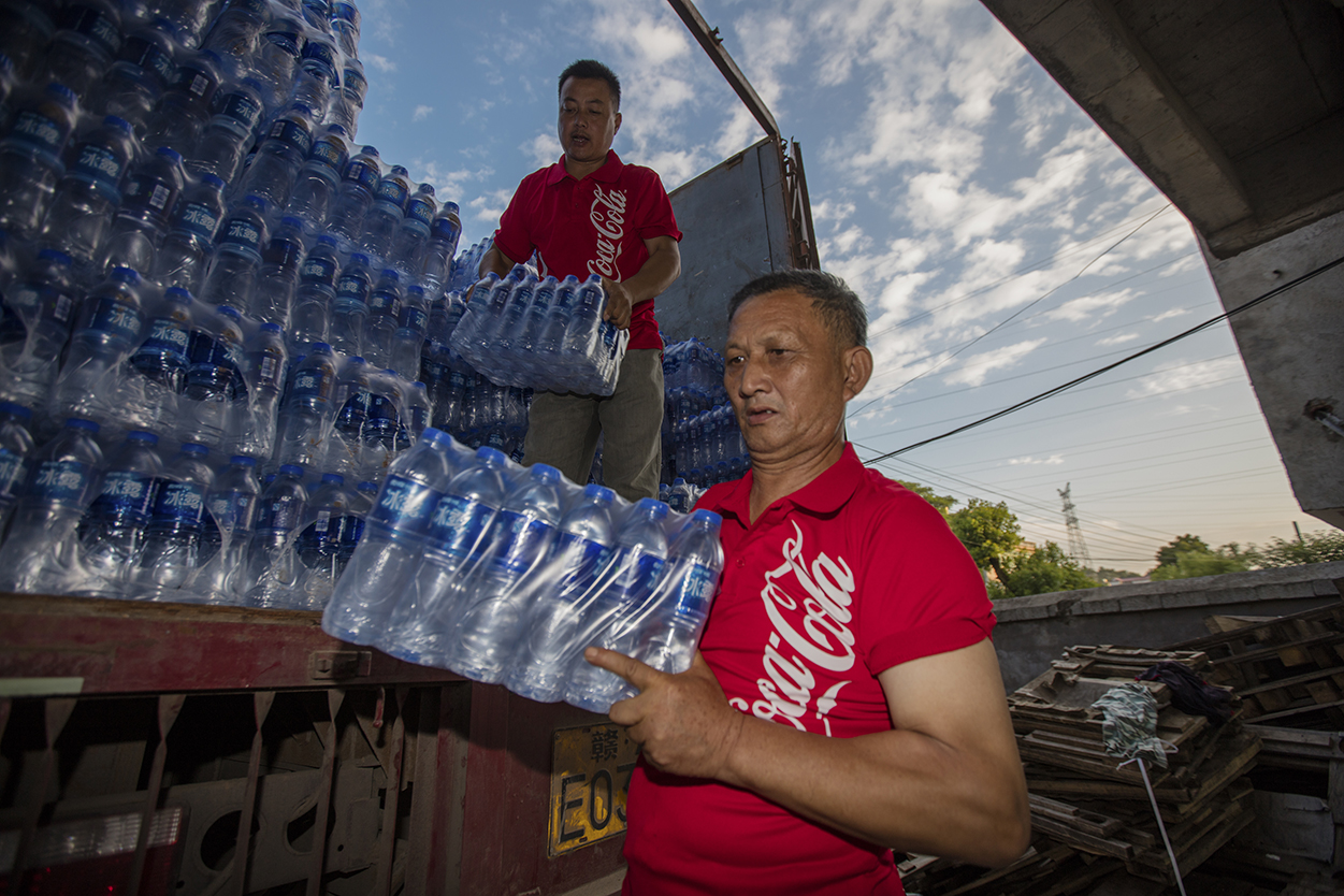 Two men unloading packages of bottled water from a truck