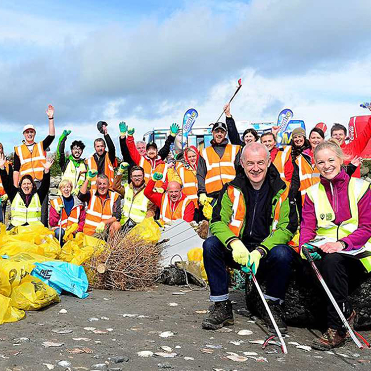 A large group of individuals wearing safe vests posing with yellow plastic bags and waste collection tools