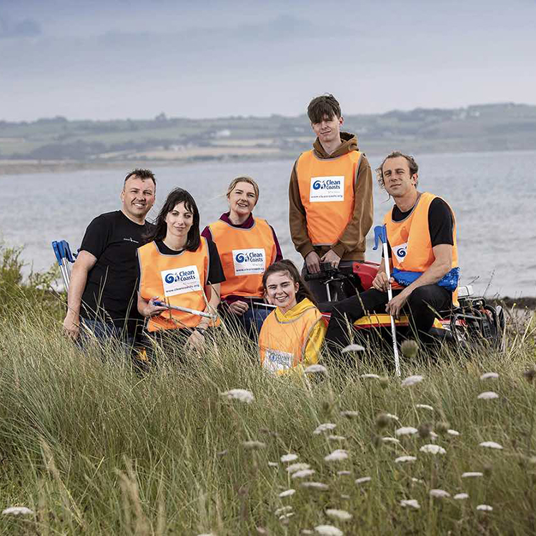 A group of six people wearing orange vests posing in front of a shoreline landscape