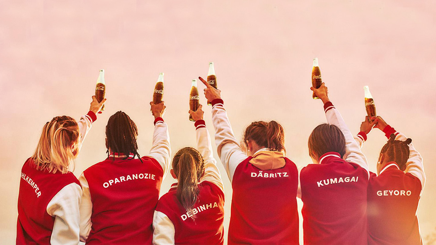 Six women with red jackets holding Coca-Cola bottles