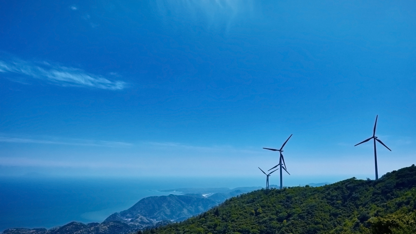 写真：青空の下、海を見渡す丘に立つ三つの風力発電機