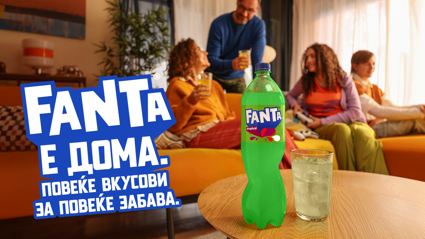 Familja është ulur në dhomën e ndenjës, luan video‑lojëra dhe shijon pijen, ndërsa shishja e Fantës me portokall është e theksuar në plan të parë si simbol i momenteve të përbashkëta dhe shijes së shkëlqyer.