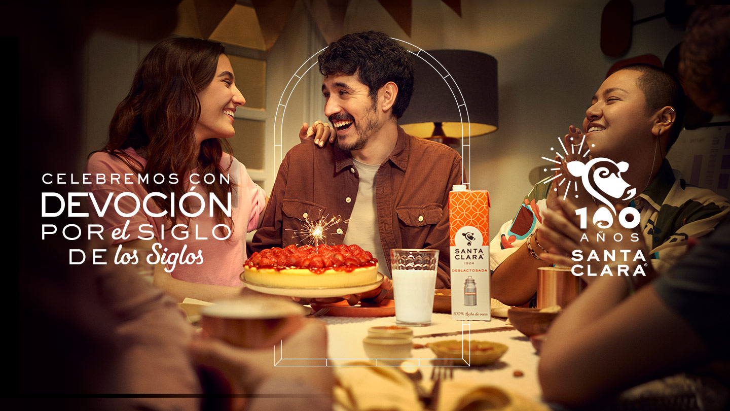 Grupo de amigos sonrientes celebrando alrededor de un pastel de fresas, con leche Santa Clara en la mesa. Texto '100 Años Santa Clara' y 'Celebremos con Devoción por el Siglo de los Siglos.