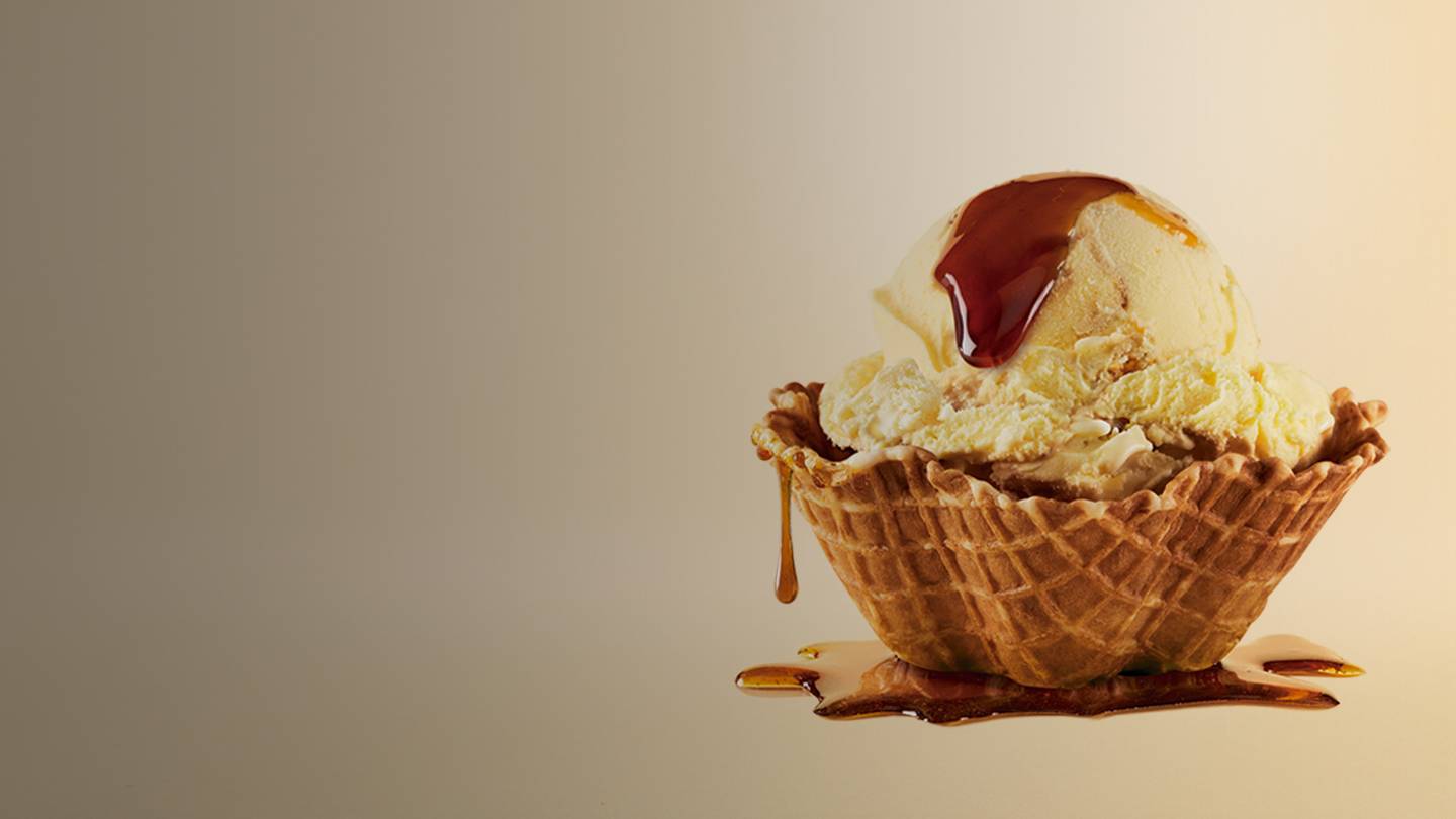 Imagen promocional de un nuevo sabor de helado llamado 'Delirio Celestial Banoffee'. Se ve una bola de helado cremoso con trozos de plátano, salsa de caramelo y pedazos de galleta, todo sobre un fondo claro y brillante. El texto 'Nuevo Sabor' resalta en la parte superior.