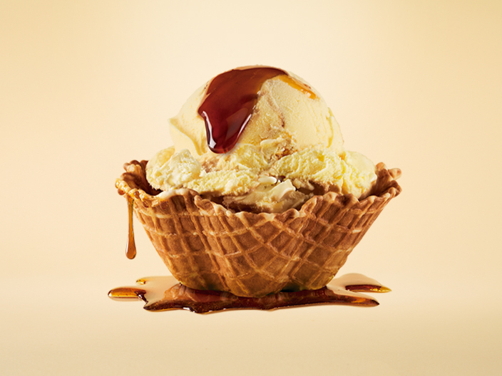 Imagen de una bola de helado Santa Clara, nuevo sabor, adornada con plátano, caramelo líquido y trozos de galleta. Se destaca el texto 'Nuevo Sabor' y el logo de Santa Clara.