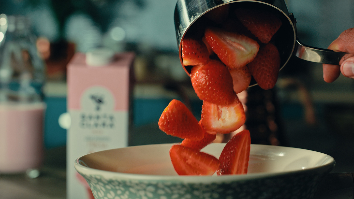 Fresas frescas cayendo en un tazón grande, con un fondo borroso de cocina y un cartón de leche rosa de Santa Clara.