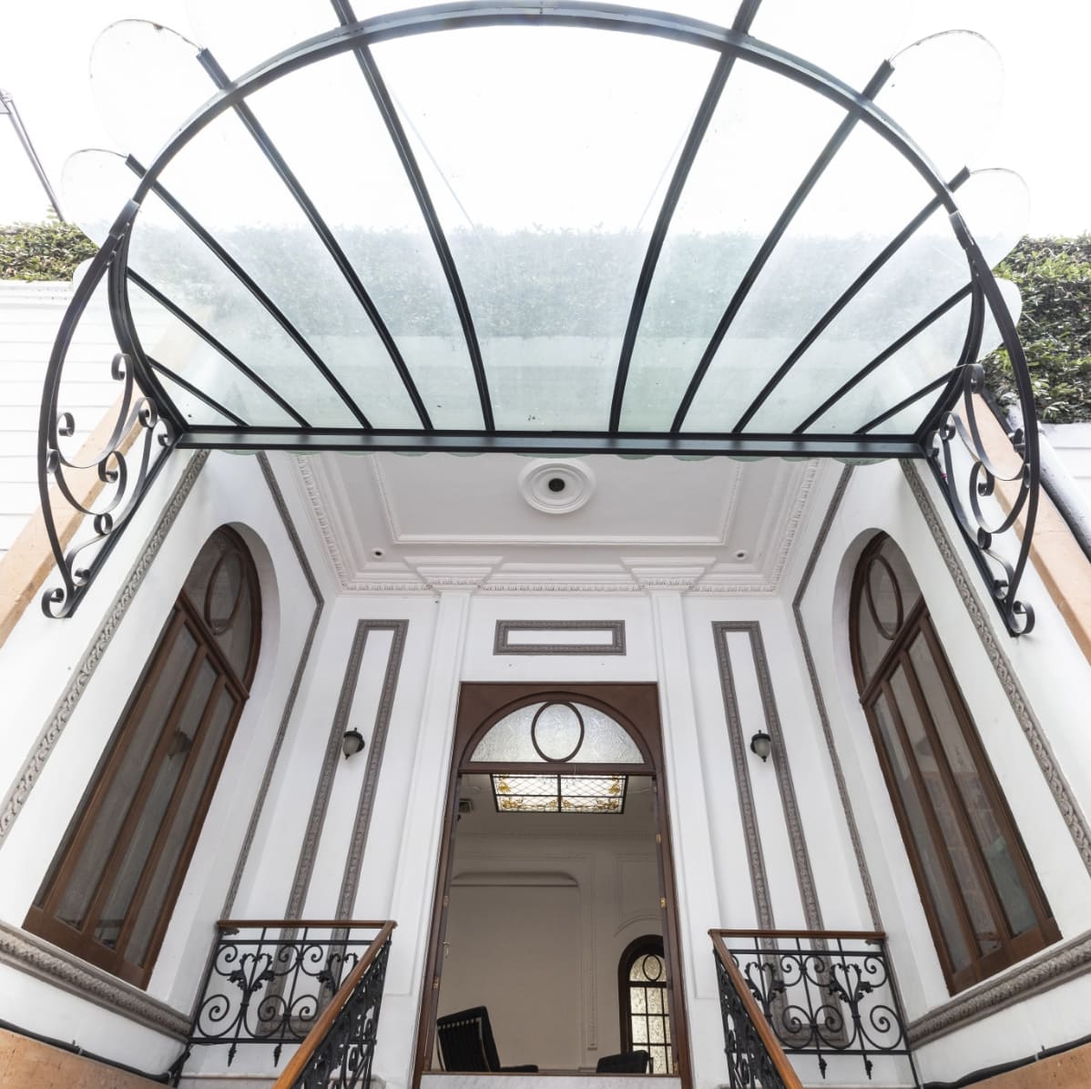 Un elegante edificio blanco con un toldo de cristal sobre la entrada y barandillas de hierro forjado a ambos lados de las escaleras.