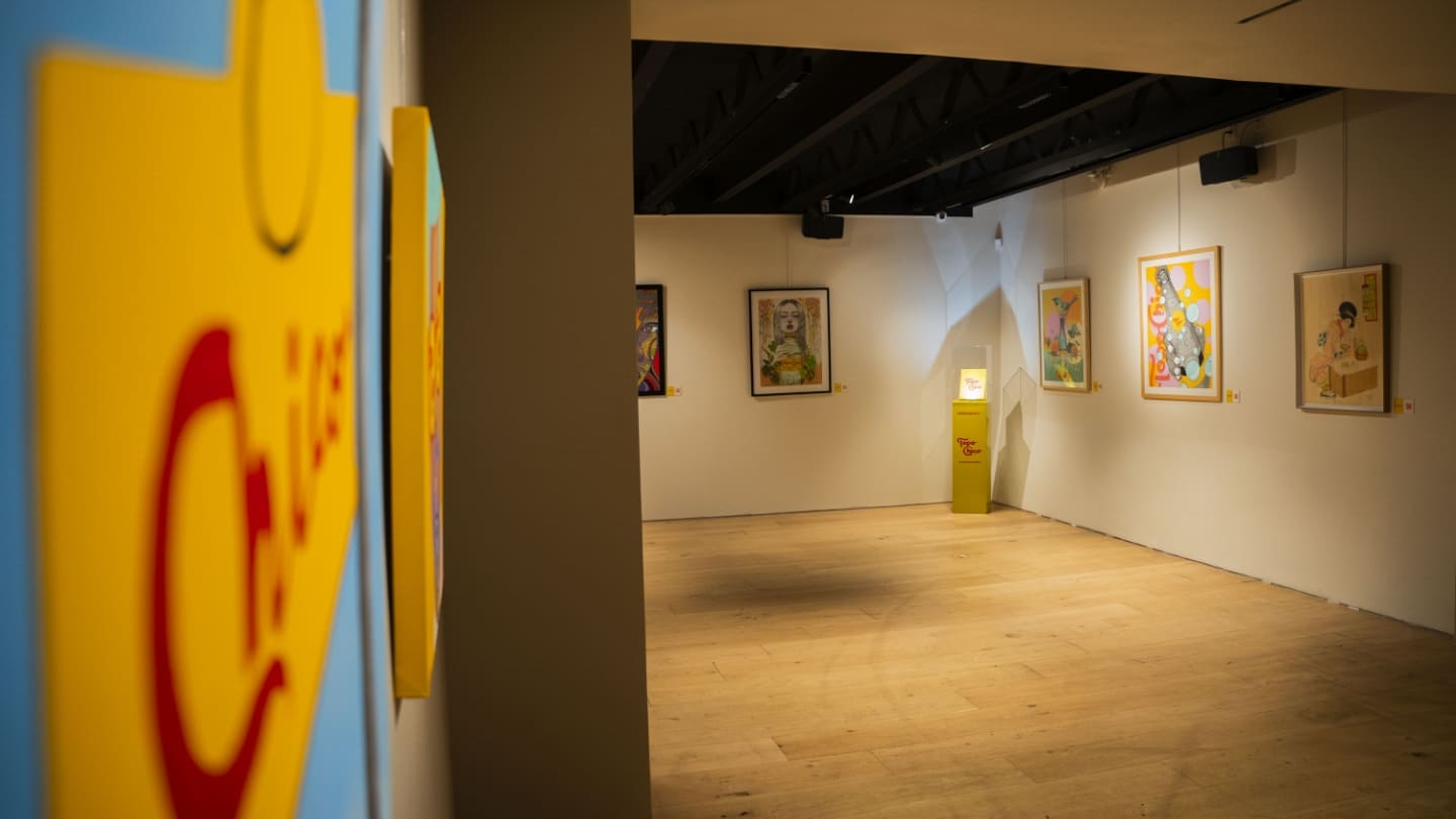 Una exposición de arte con cuadros de colores en las paredes y un pedestal amarillo en el centro de la sala.