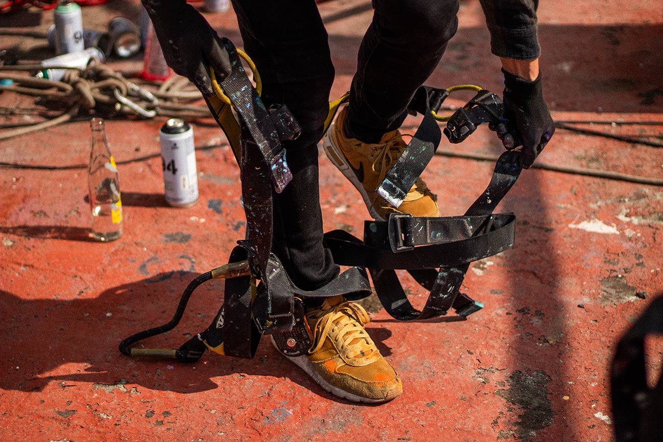 Persona quitándose el arnés. Tiene zapatillas de color amarillas y de fondo se ve una botella de vidrio Topo Chico y una lata de color blanco.