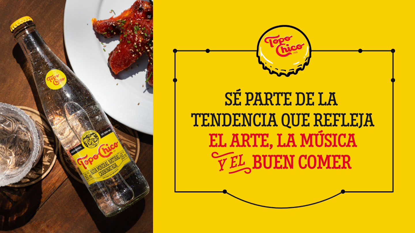 Botella de Topo Chico sobre una mesa de madera. Se observa la leyenda "Se parte de la tendencia que refleja el arte, la musica y el buen comer" y el logotipo de Topo Chico sobre un fondo amarillo.