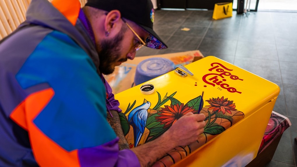 Diseñador pintando en una heladera Topo Chico de color amarillo y flores de color rojo y hojas verdes